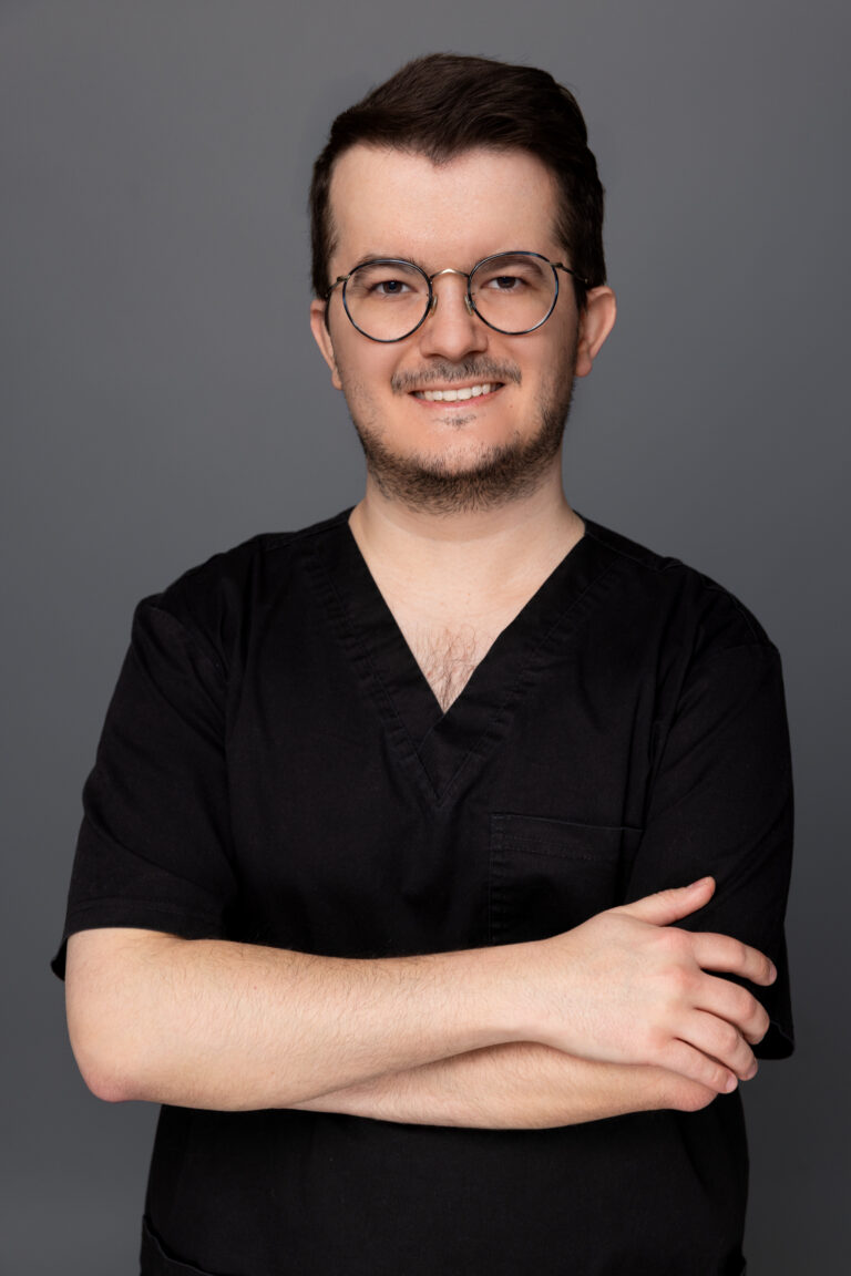Lekarz stomatolog w czarnym stroju, uśmiechnięty portret na stronie naszego zespołu